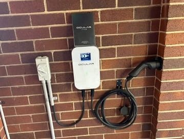 White EV charger mounted on an exterior brick wall with charging cable coiled beside it.