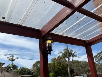 Black outdoor light mounted to a timber post beneath a covered outdoor area.