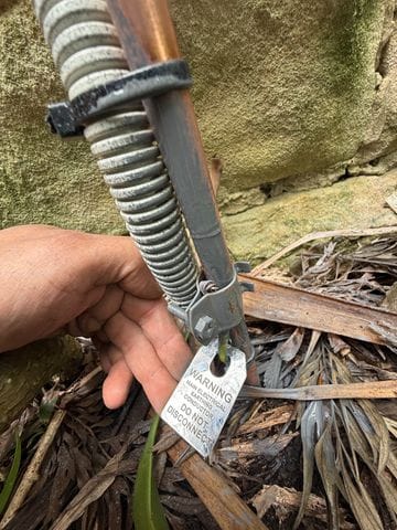 Electrical earth cable and earth stake installed beside an exterior brick wall.