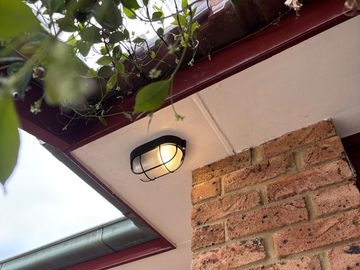 Black outdoor light mounted beneath the eaves above a brick wall.